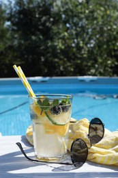 Photo of Tasty cocktail in glass and sunglasses near swimming pool outdoors