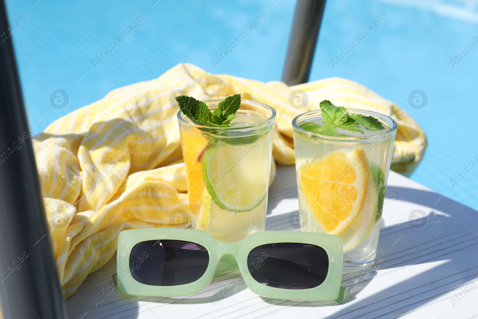 Photo of Tasty cocktail in glasses and sunglasses near swimming pool outdoors