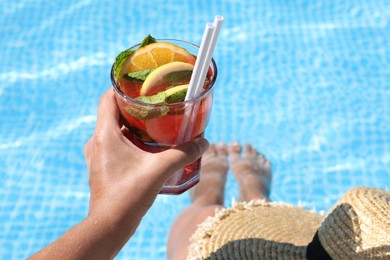 Photo of Woman holding tasty cocktail in glass near swimming pool outdoors, closeup