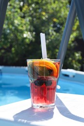 Photo of Tasty cocktail in glass near swimming pool outdoors