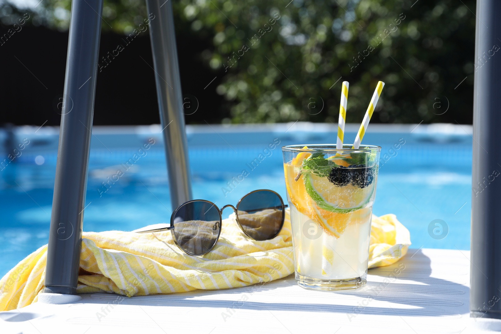 Photo of Tasty cocktail in glass and sunglasses near swimming pool outdoors