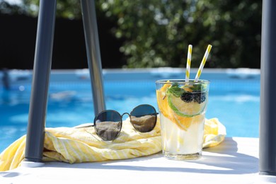 Photo of Tasty cocktail in glass and sunglasses near swimming pool outdoors