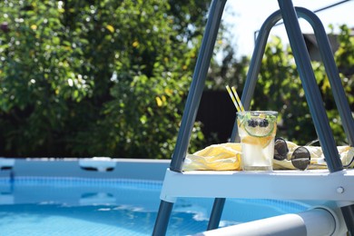 Photo of Tasty cocktail in glass and sunglasses near swimming pool outdoors, space for text