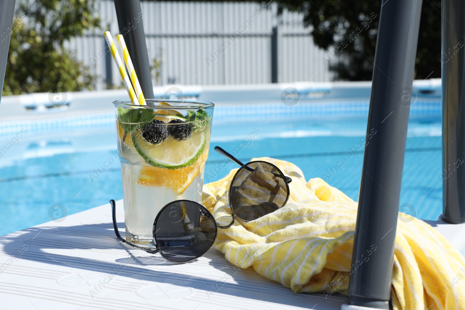 Photo of Tasty cocktail in glass and sunglasses near swimming pool outdoors