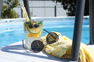 Photo of Tasty cocktail in glass and sunglasses near swimming pool outdoors