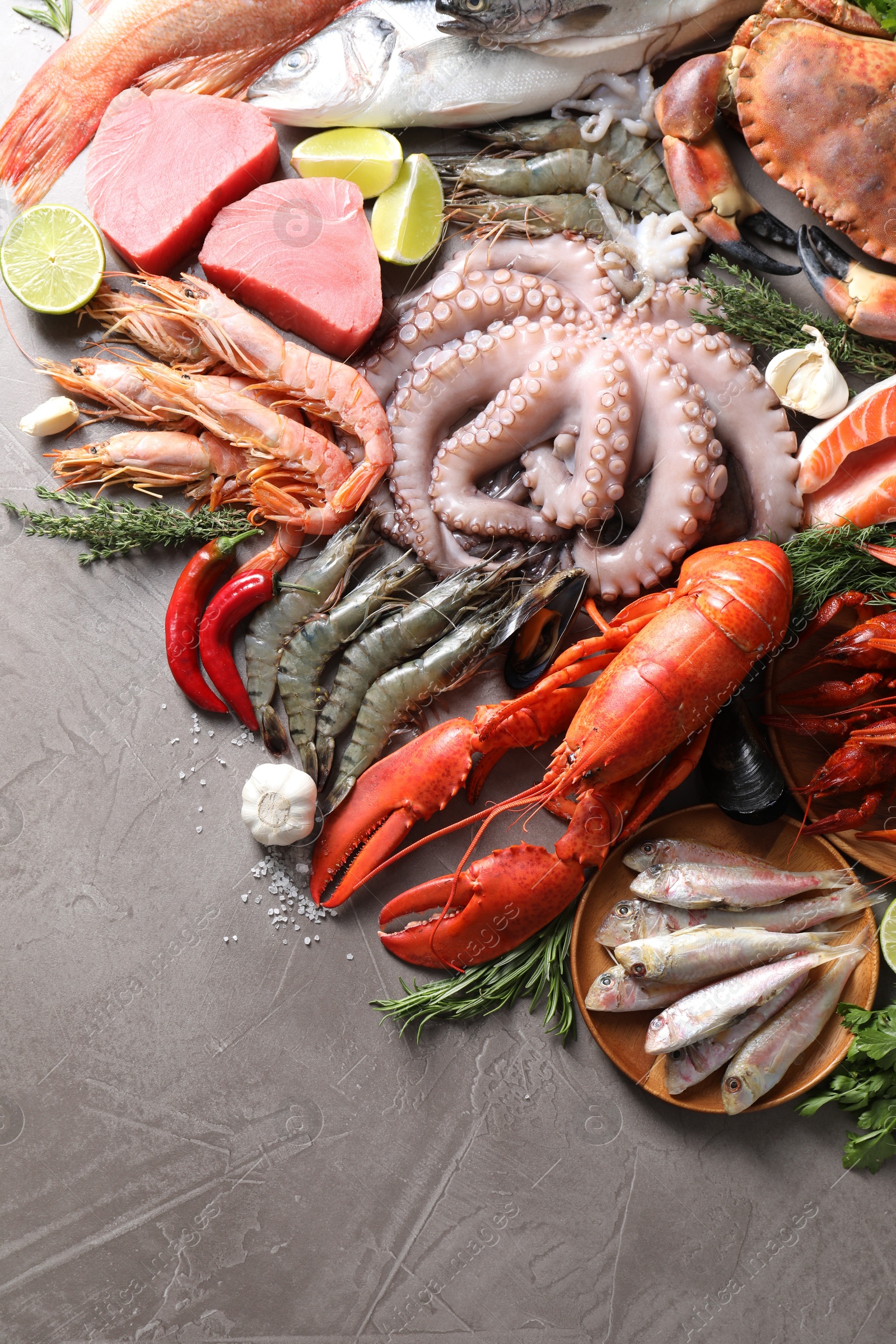 Photo of Many different sea food, herbs, garlic and lime on grey table, flat lay. Space for text