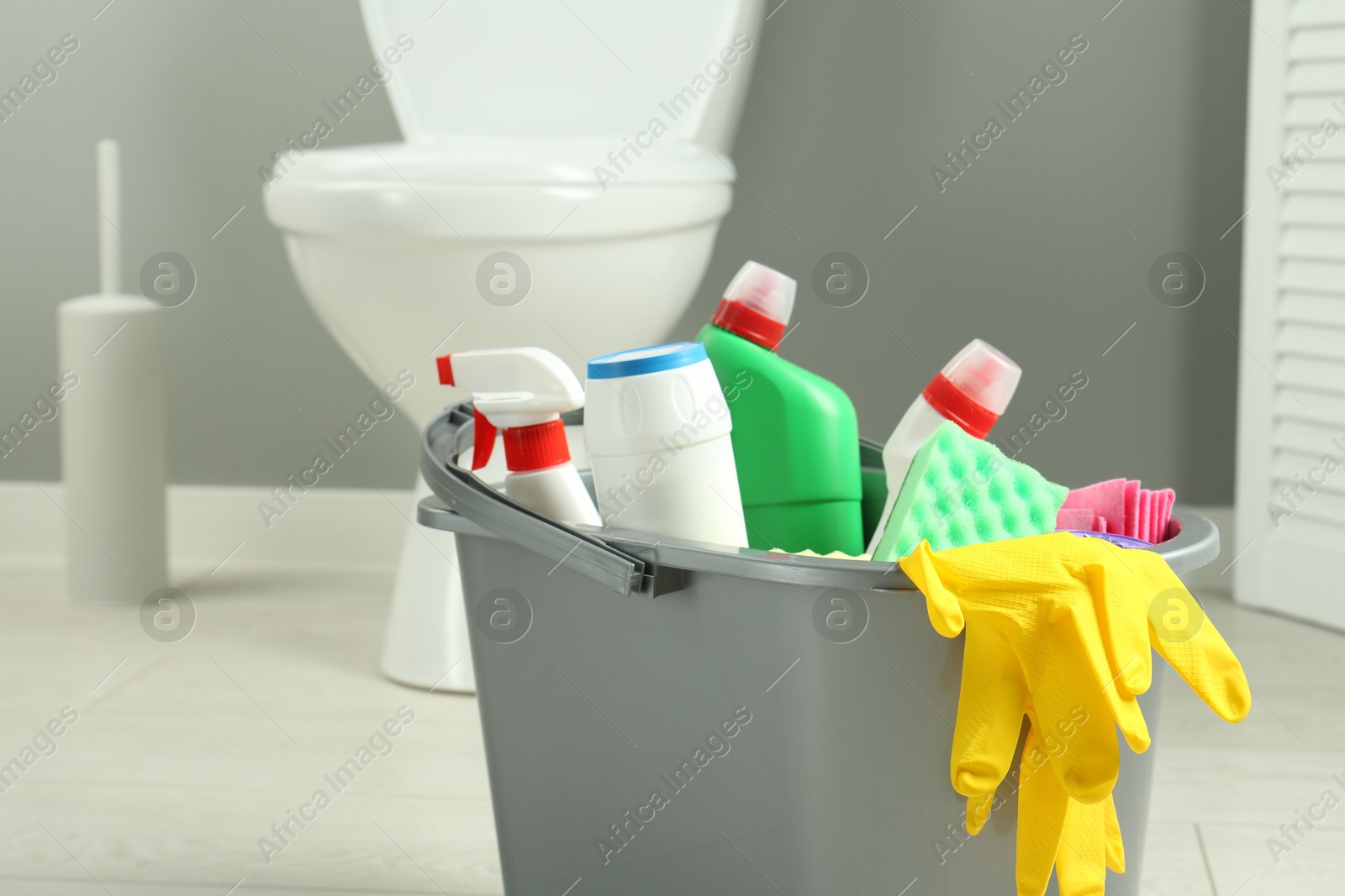 Photo of Bucket with different toilet cleaners, rag, sponge and gloves in bathroom