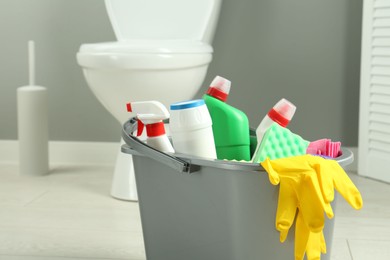 Photo of Bucket with different toilet cleaners, rag, sponge and gloves in bathroom