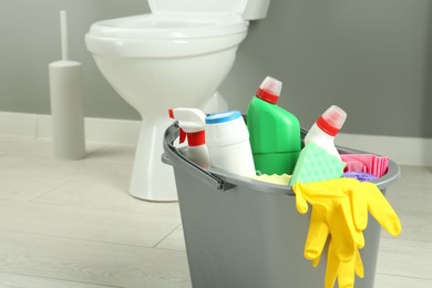 Photo of Bucket with different toilet cleaners, rag, sponge and gloves in bathroom