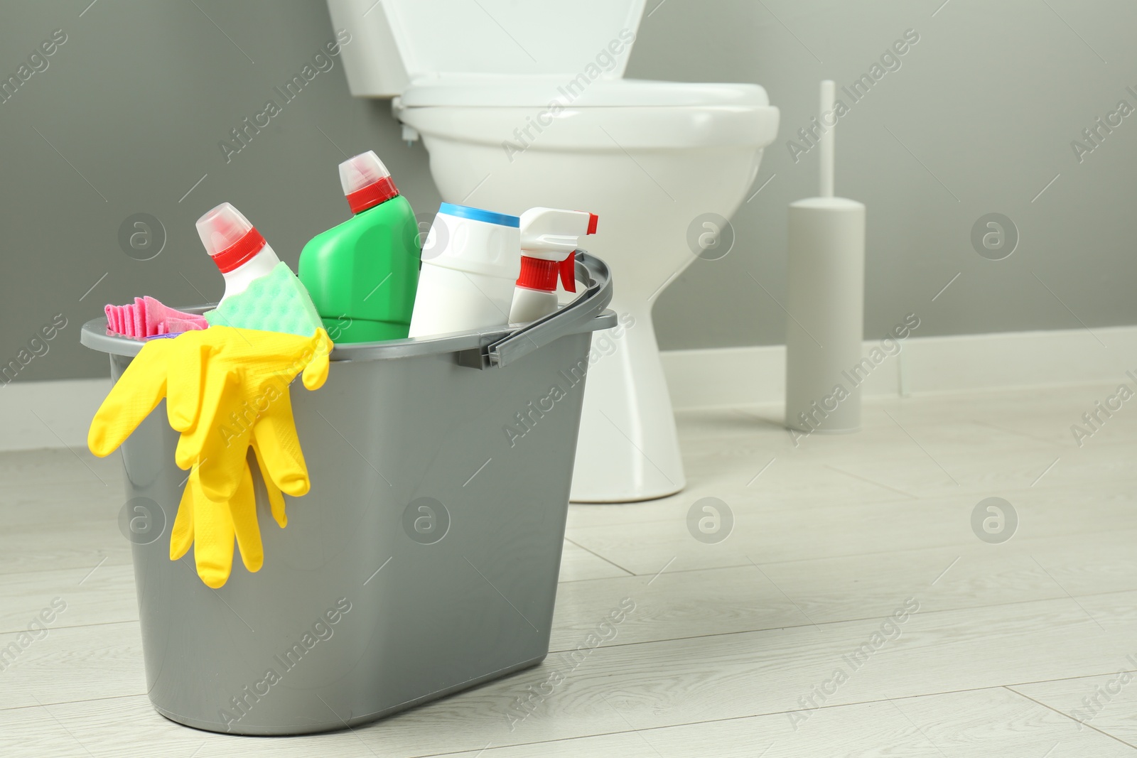 Photo of Bucket with different toilet cleaners, rag, sponge and gloves in bathroom