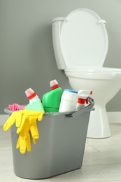 Photo of Bucket with different toilet cleaners, rag, sponge and gloves in bathroom