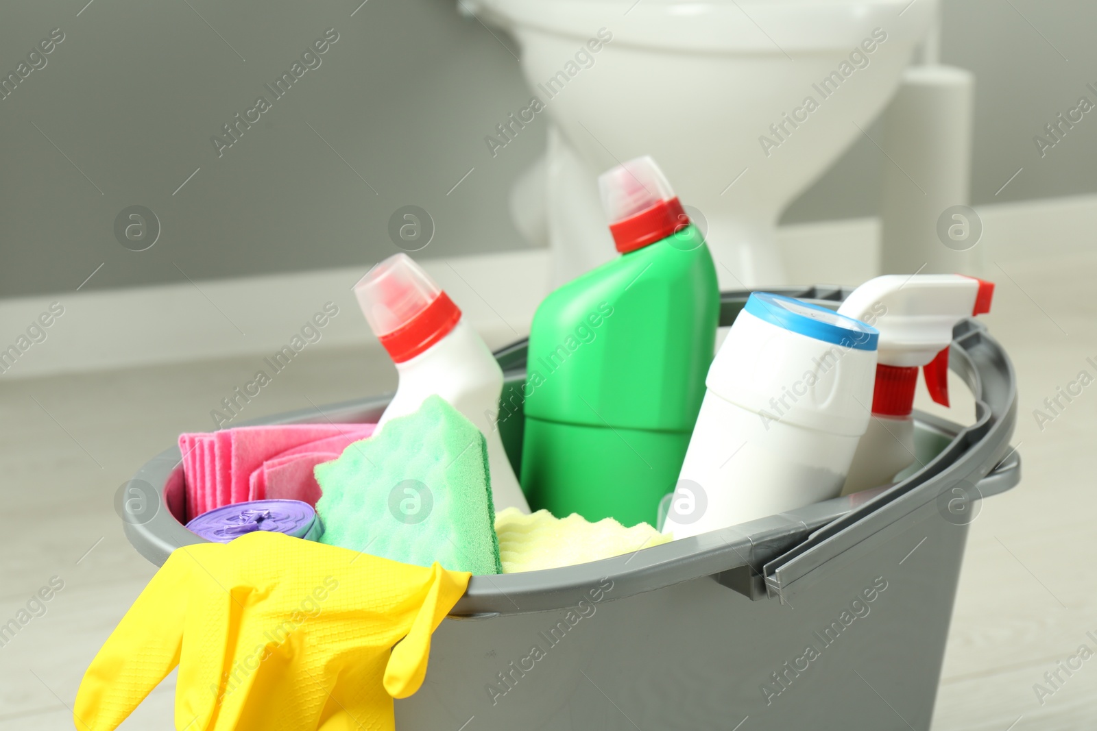 Photo of Bucket with different toilet cleaners, sponges, rag and gloves in bathroom, closeup