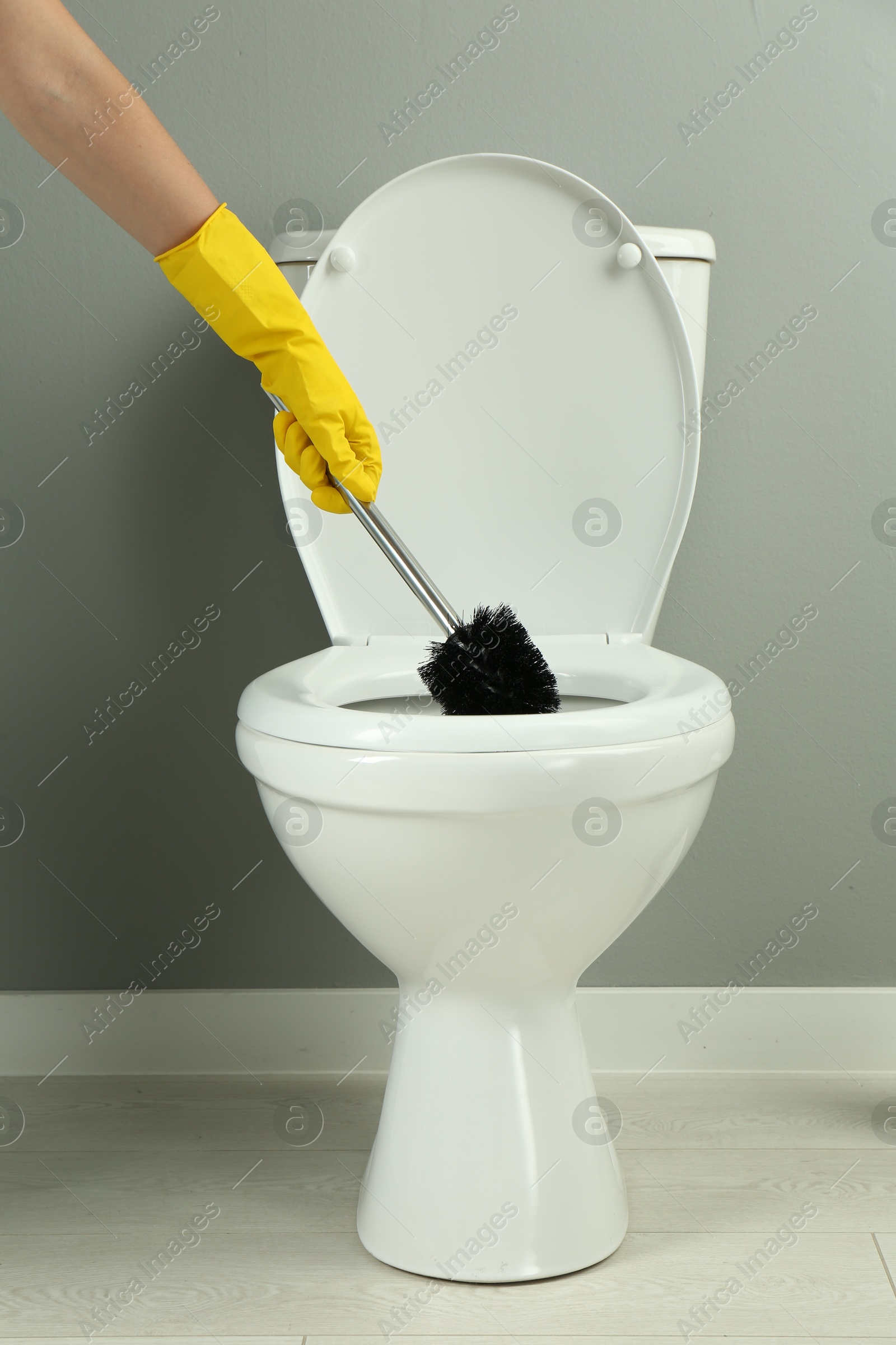 Photo of Woman cleaning toilet with brush in bathroom, closeup