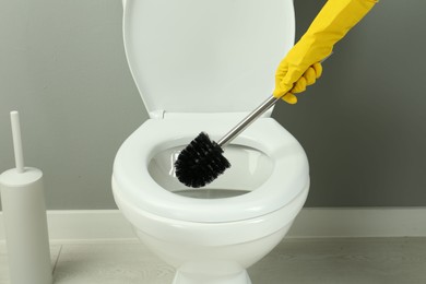 Photo of Woman cleaning toilet with brush in bathroom, closeup