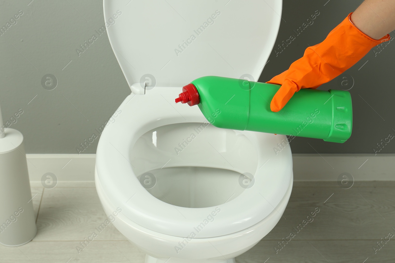 Photo of Woman cleaning toilet with detergent in bathroom, closeup