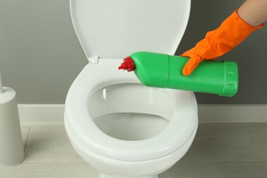 Photo of Woman cleaning toilet with detergent in bathroom, closeup