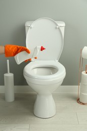 Photo of Woman cleaning toilet with detergent in bathroom, closeup