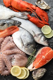 Whole fresh raw octopus, fish and other sea food on black table, flat lay