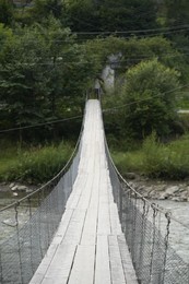 Photo of View of wooden suspension bridge over mountain river