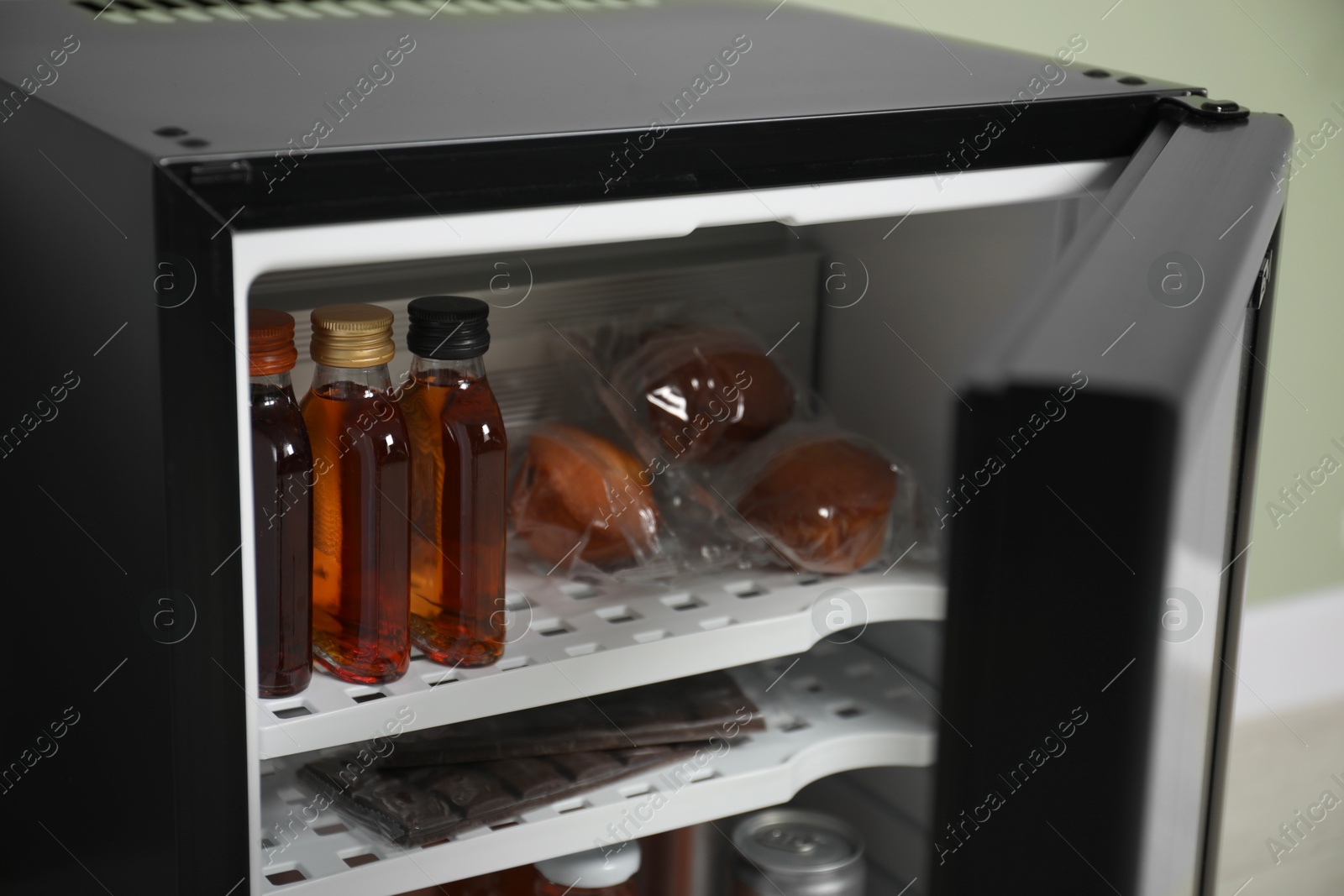 Photo of Mini refrigerator with different drinks and snacks indoors, closeup