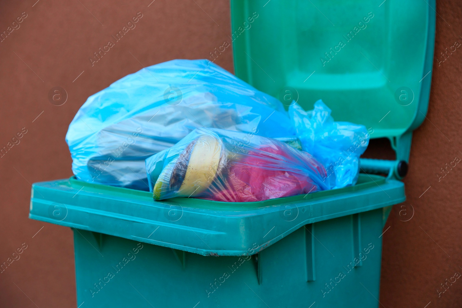 Photo of Trash bags in garbage bin near brown wall outdoors, closeup