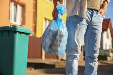 Man with trash bag full of garbage and bin outdoors, closeup