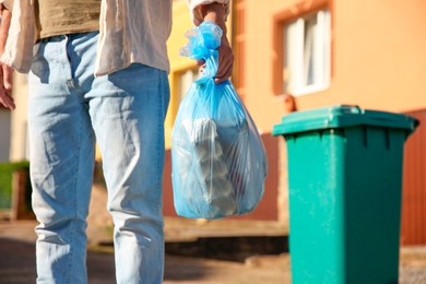 Man with trash bag full of garbage and bin outdoors, closeup