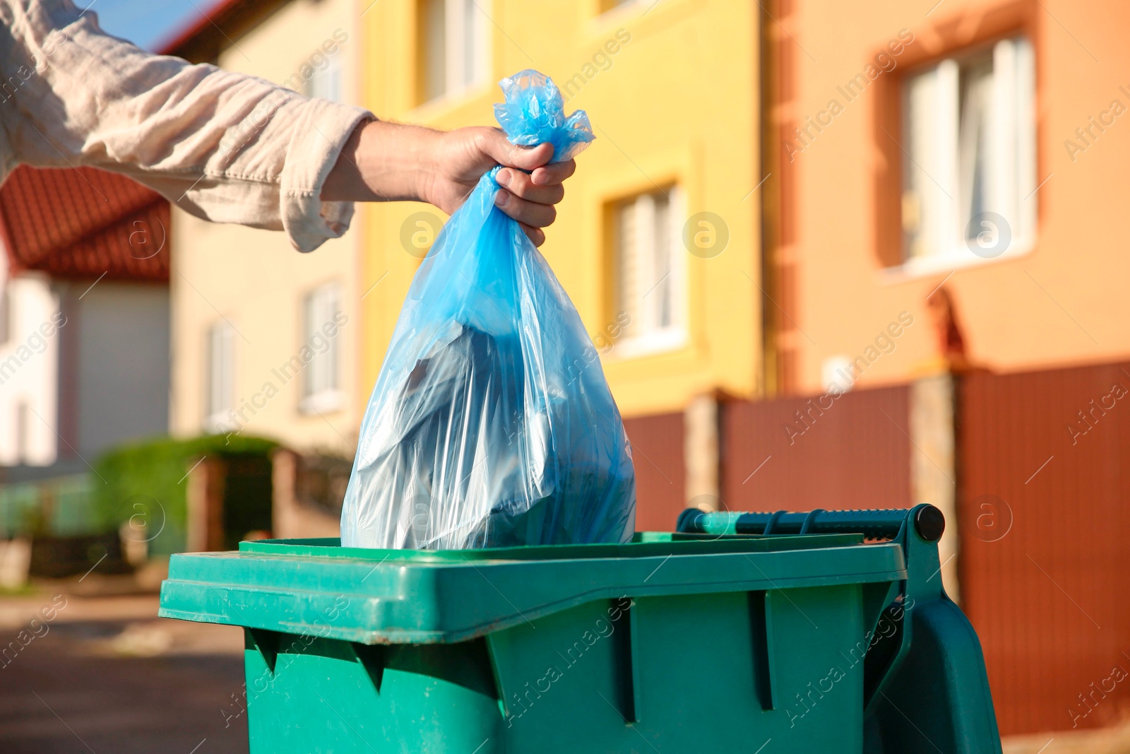 Photo of Man throwing trash bag into bin outdoors, closeup