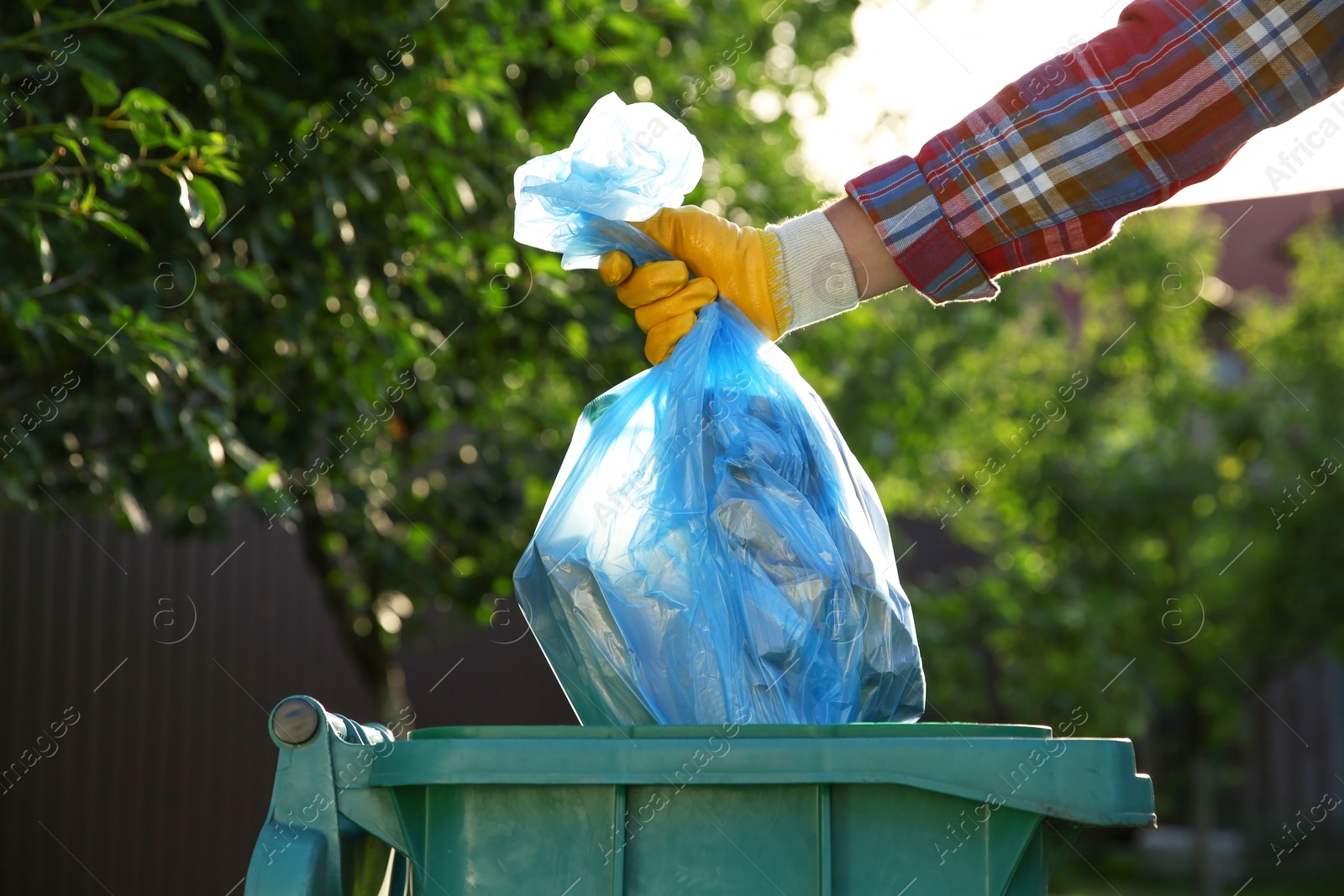 Photo of Man throwing trash bag into bin outdoors, closeup