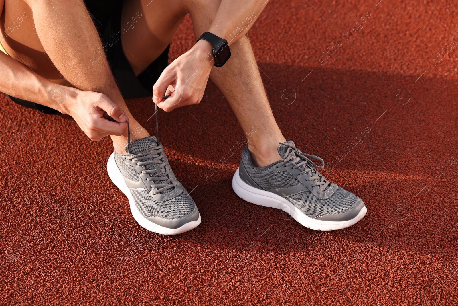 Photo of Man tying shoelace of grey sneaker at stadium, closeup