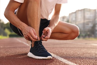 Photo of Man tying shoelace of black sneaker at stadium, closeup