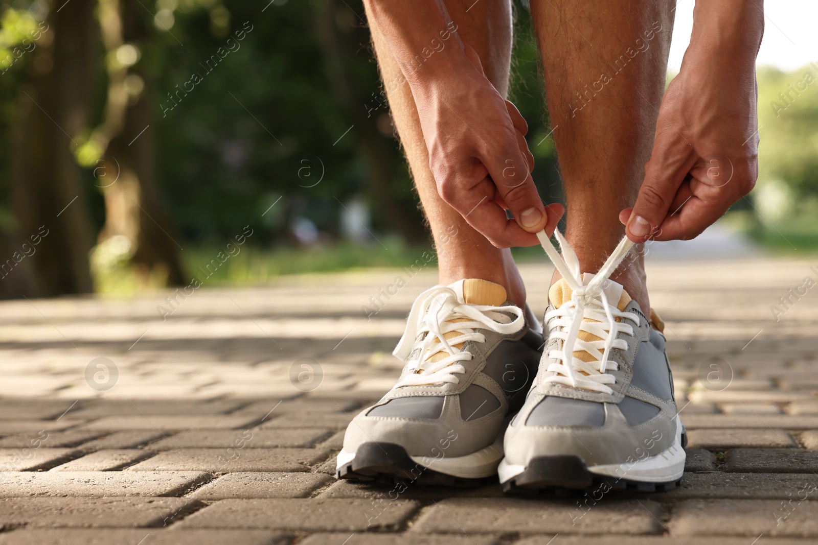 Photo of Man tying shoelace of grey sneaker outdoors, closeup. Space for text