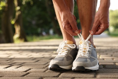 Photo of Man tying shoelace of grey sneaker outdoors, closeup. Space for text