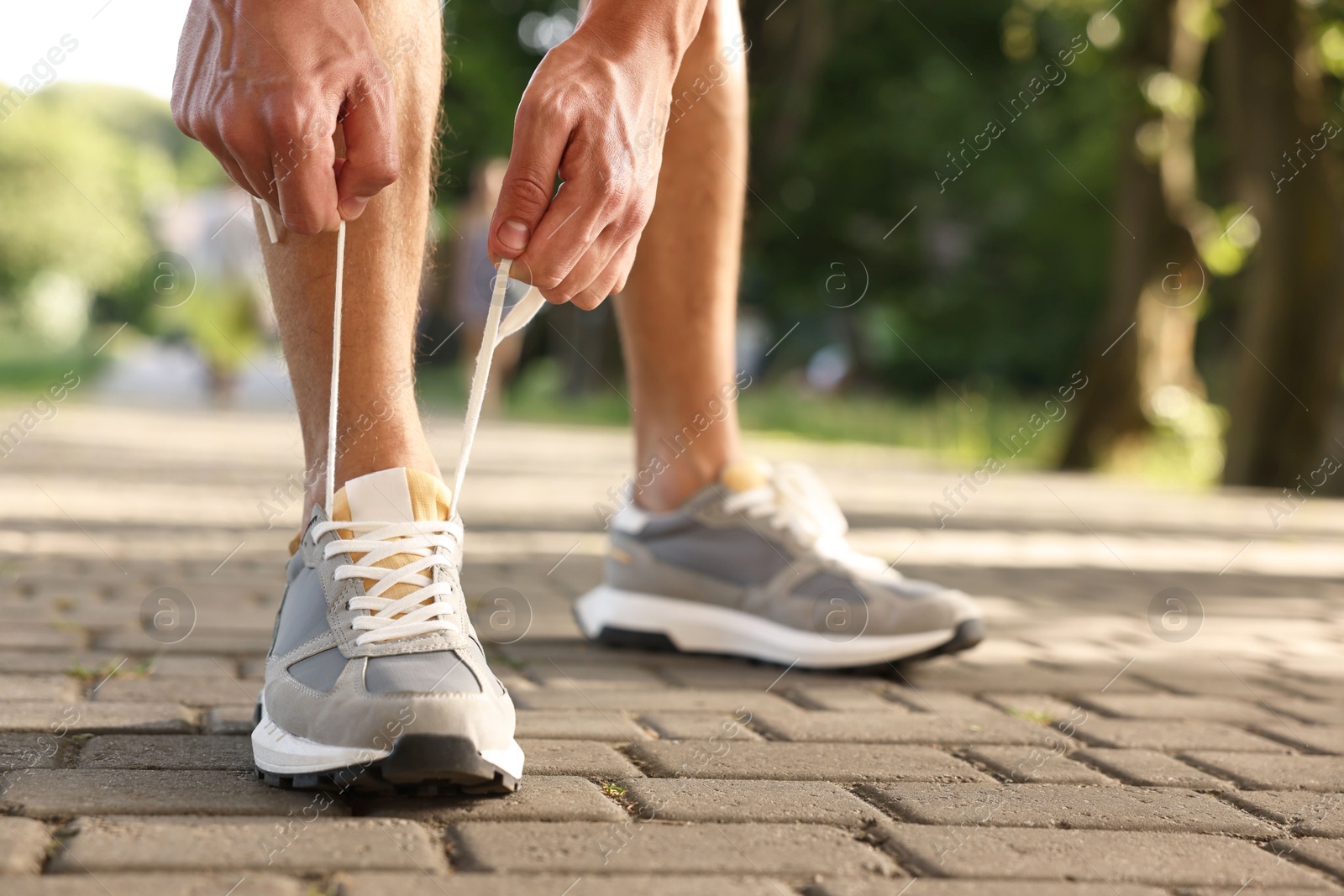 Photo of Man tying shoelace of grey sneaker outdoors, closeup. Space for text