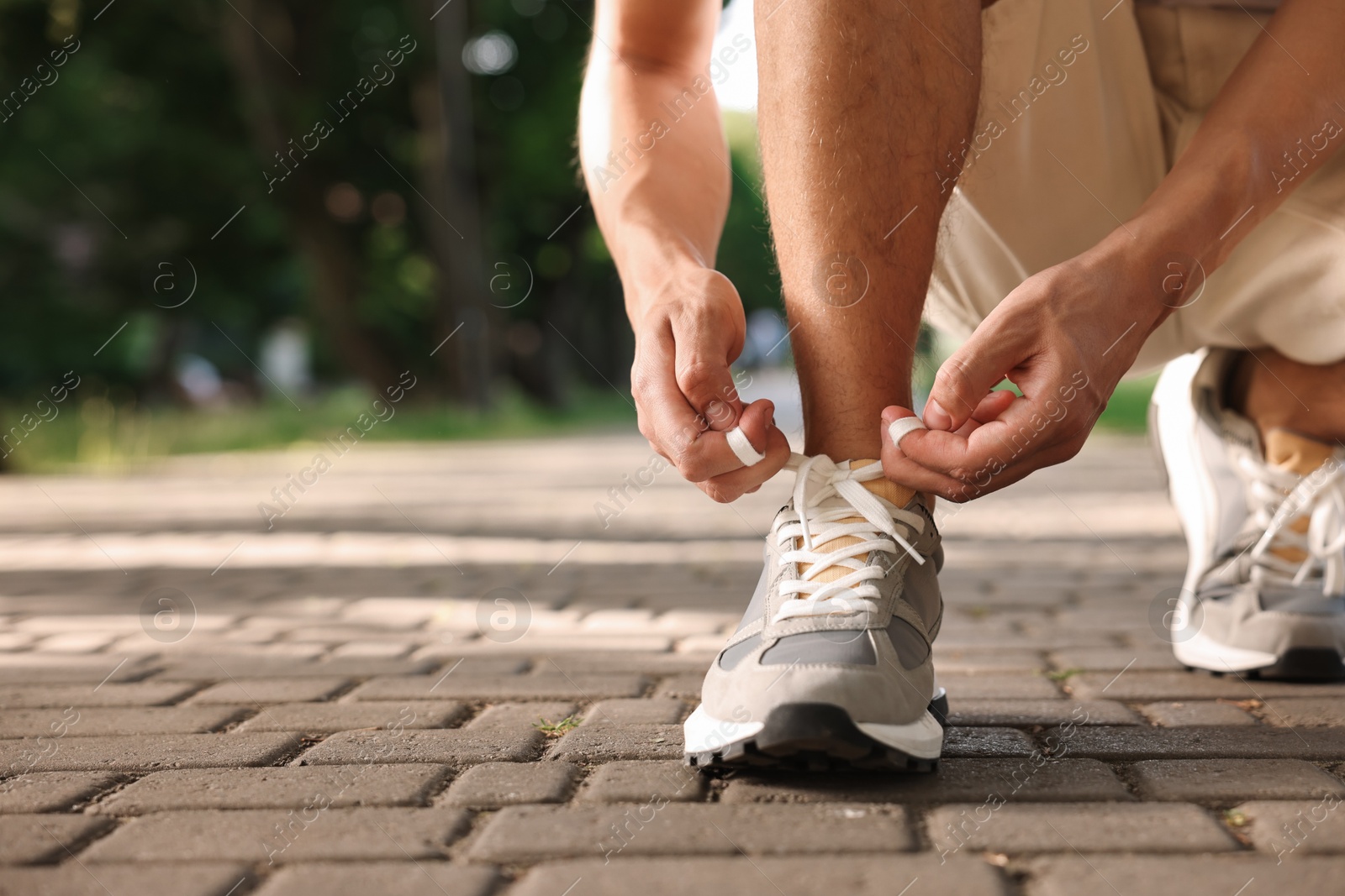 Photo of Man tying shoelace of grey sneaker outdoors, closeup. Space for text