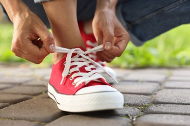 Woman tying shoelace of red sneaker outdoors, closeup