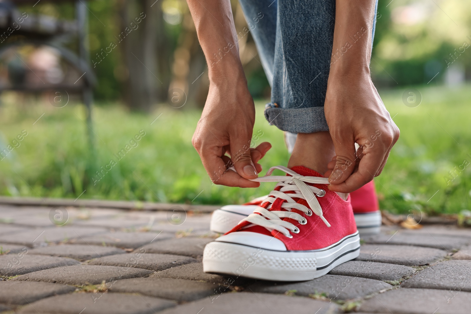 Photo of Woman tying shoelace of red sneaker outdoors, closeup. Space for text