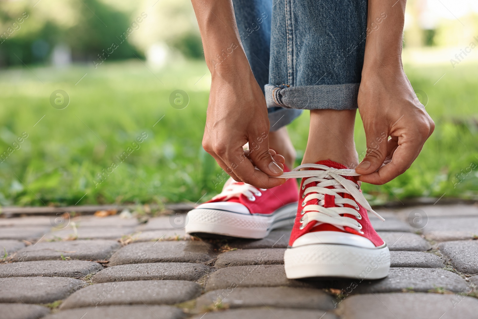 Photo of Woman tying shoelace of red sneaker outdoors, closeup. Space for text