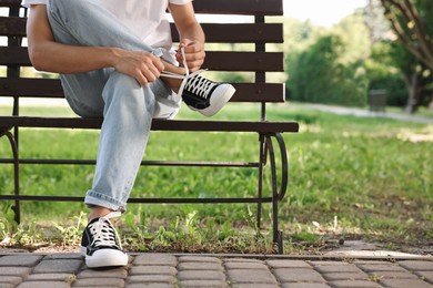 Photo of Man tying shoelace of black sneaker on bench outdoors, closeup. Space for text