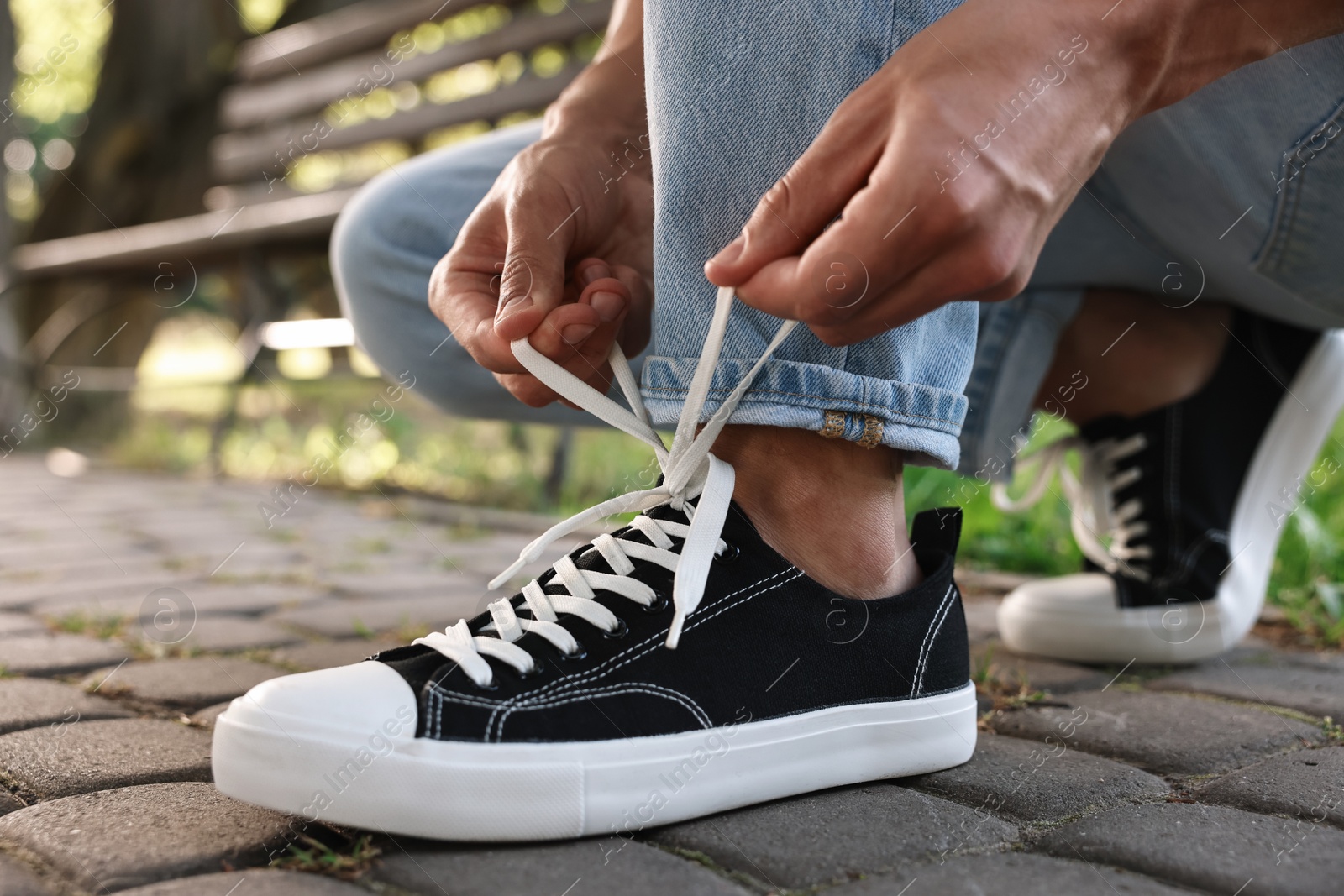 Photo of Man tying shoelace of black sneaker outdoors, closeup