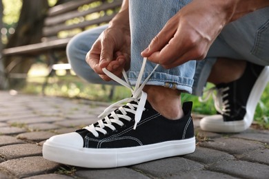 Photo of Man tying shoelace of black sneaker outdoors, closeup