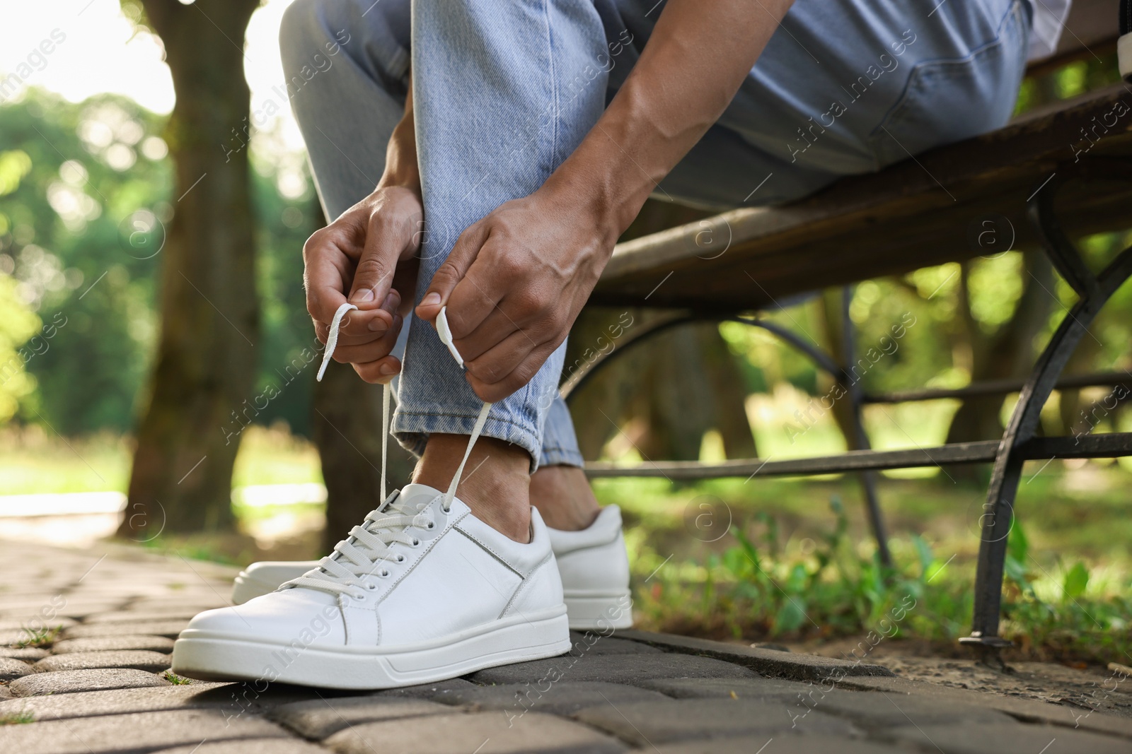 Photo of Man tying shoelace of white sneaker outdoors, closeup