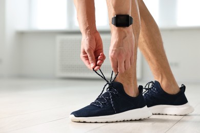 Man tying shoelace of sneaker indoors, closeup. Space for text