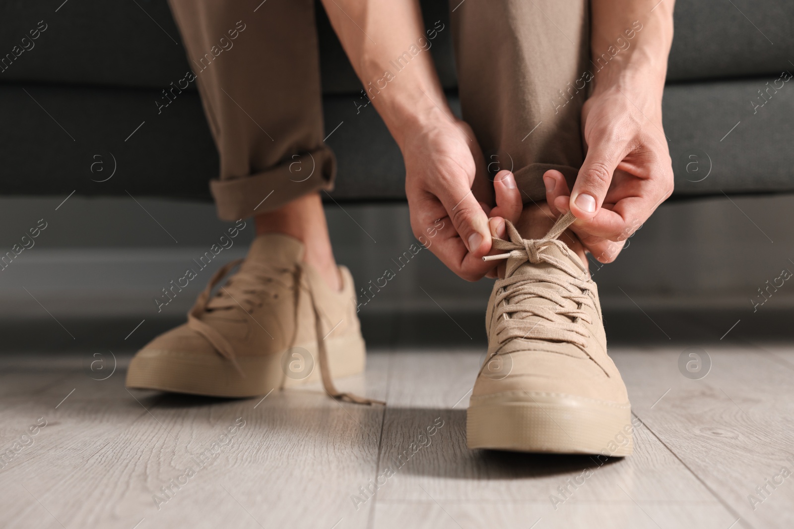 Photo of Man tying shoelace of sneaker on sofa indoors, closeup