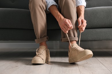 Photo of Man tying shoelace of sneaker on sofa indoors, closeup