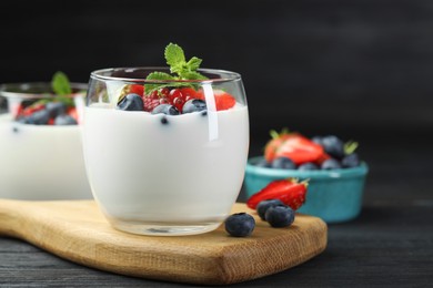 Photo of Tasty yogurt with fresh berries and mint in glasses on black wooden table, closeup