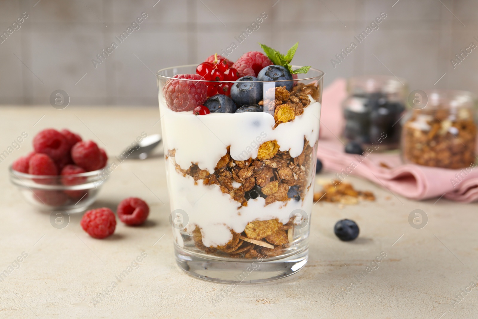 Photo of Tasty yogurt with fresh berries, granola and mint in glass on gray textured table