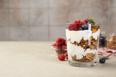 Photo of Tasty yogurt with fresh berries, granola and mint in glass on gray textured table, space for text