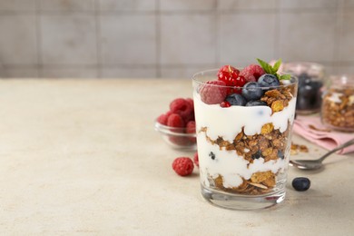 Tasty yogurt with fresh berries, granola and mint in glass on gray textured table, space for text