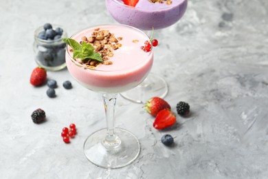 Different tasty yogurts with fresh berries and granola in glasses on gray textured table, closeup. Space for text